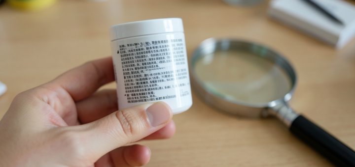 Zbliżenie na etykietę kosmetyku trzymaną w dłoni z lupą na biurku